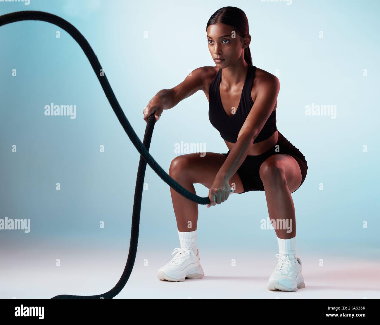 Donna, corda da battaglia o allenamento su sfondo blu in studio per l'esercizio fisico, l'allenamento o l'allenamento per i muscoli forti del braccio. Personal trainer, persona sportiva Foto Stock