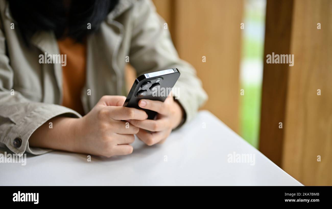 Giovane donna asiatica in abiti casual a digitare sul telefono, chattare o inviare messaggi ai suoi amici mentre si rilassa nel bar. Immagine ritagliata Foto Stock