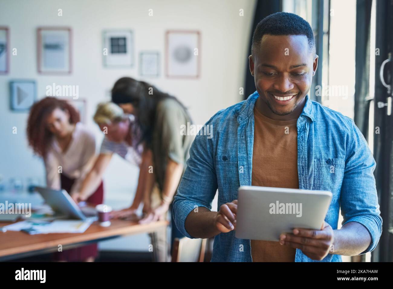 Deve avere tecnologia per l'imprenditore moderno. Un giovane uomo che utilizza un tablet digitale con il suo team sullo sfondo di un ufficio moderno. Foto Stock