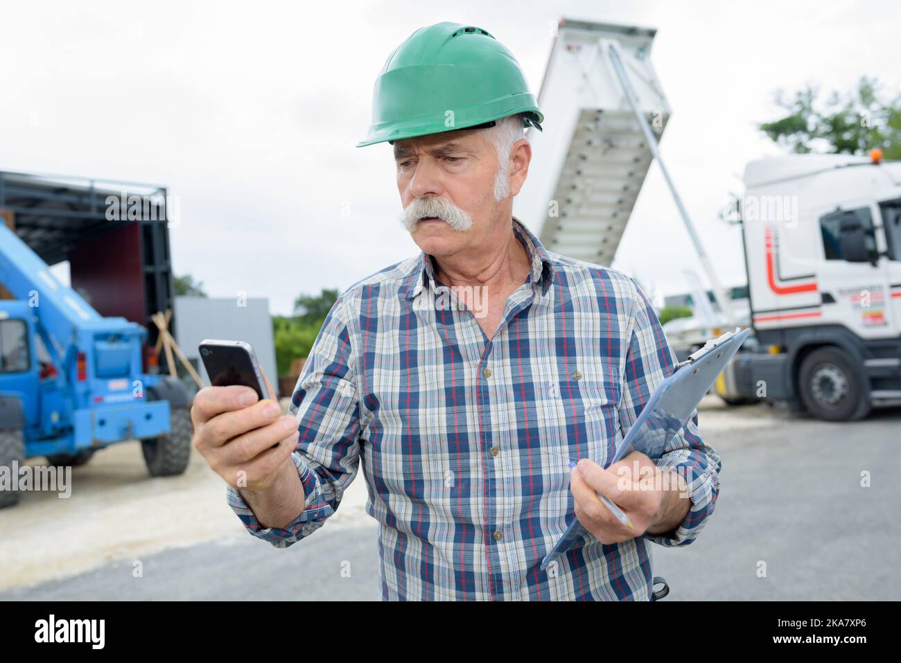uomo anziano che utilizza il camion ribaltabile smartphone scarico in background Foto Stock