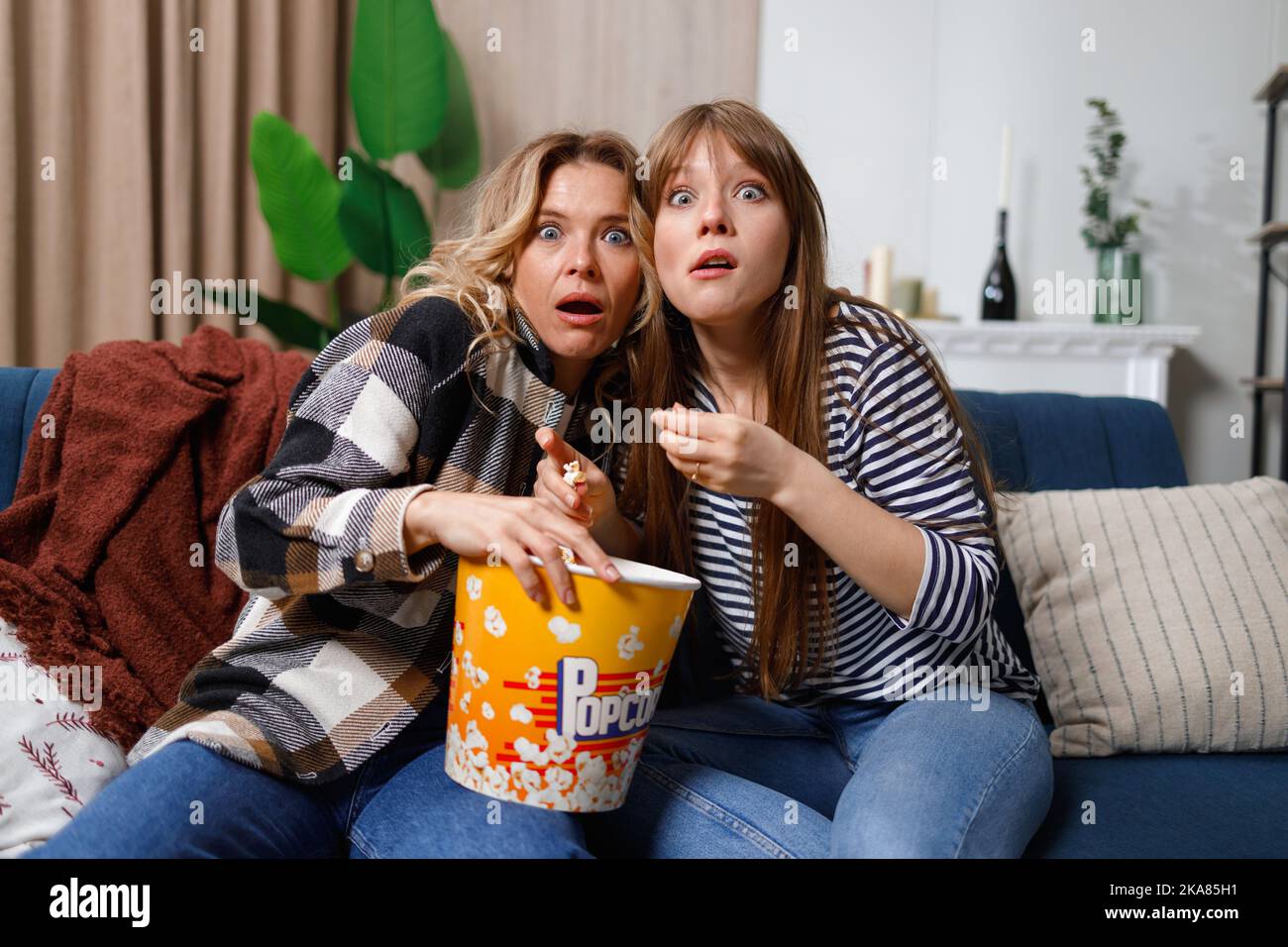 Madre e figlia si divertono a trascorrere il tempo libero a casa, guardando film spaventosi in TV e mangiando popcorn Foto Stock