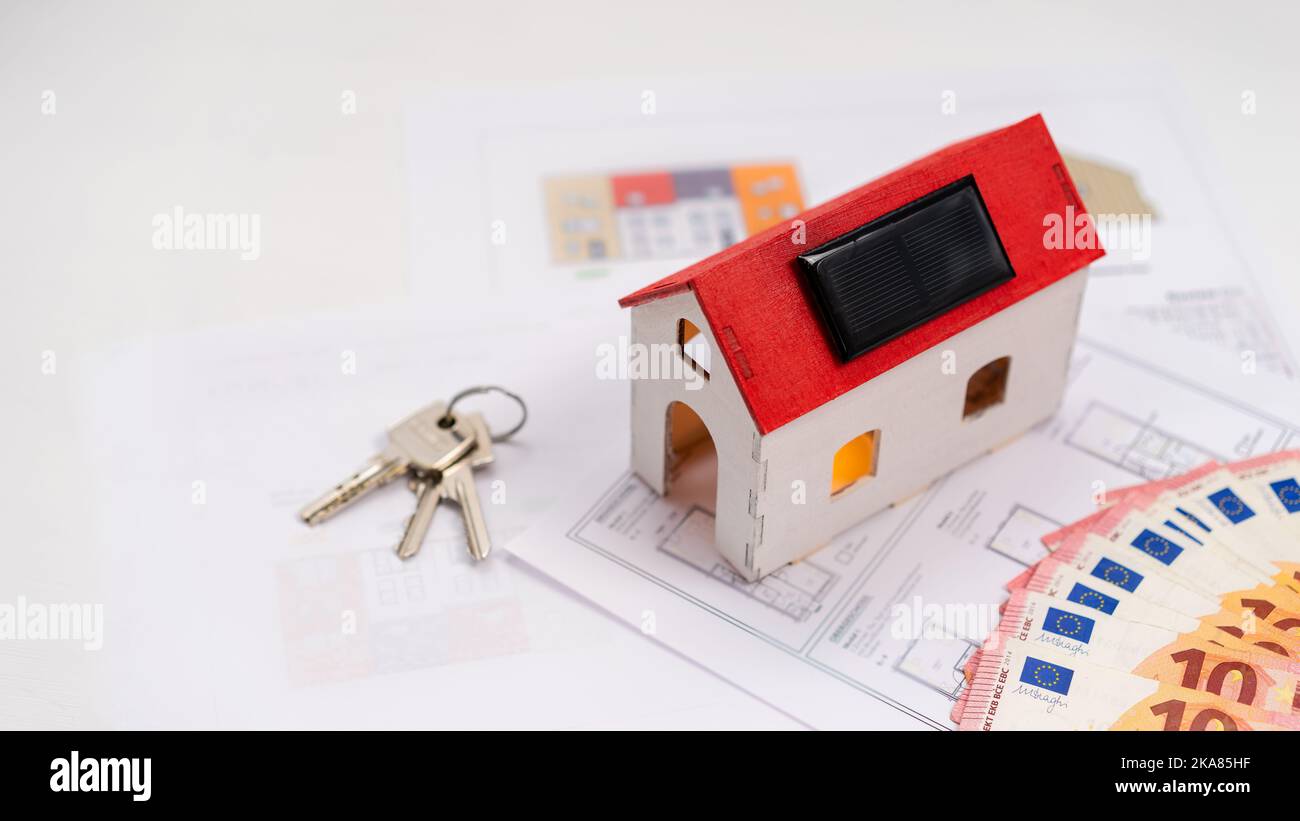 Modello casa, chiave casa e denaro su tavolo di legno. Investimento per comprare concetto di bene immobile. Primo piano del modello di casa a pannelli solari. Foto Stock