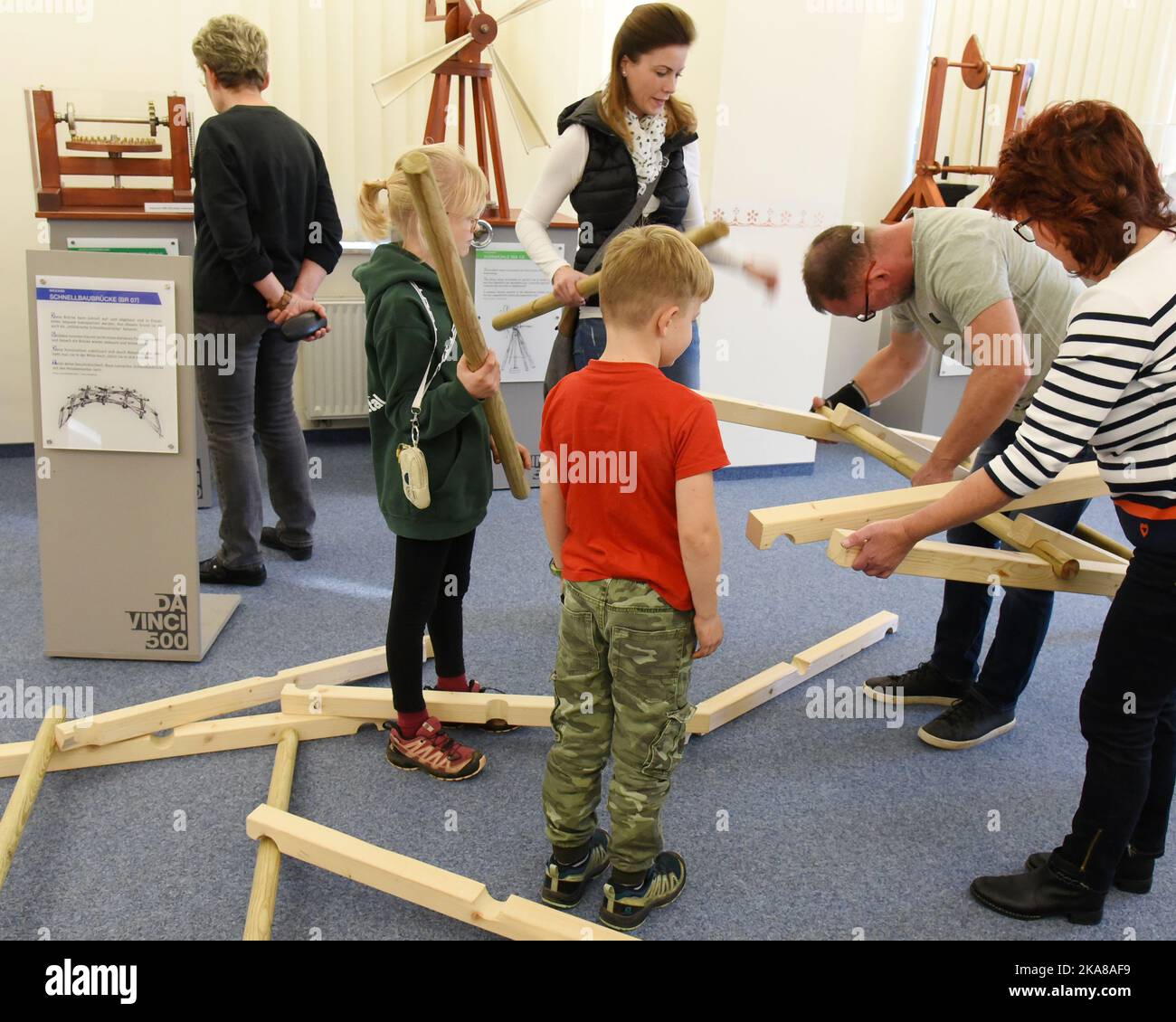 31 ottobre 2022, Sassonia, Grimma: Nella mostra "da Vinci 500 - Moving invenzioni" nel Wilhelm Ostwald Park, i visitatori riassemblano il modello di un ponte in legno autoportante, precedentemente collassato, di da Vinci (1452-1519) con l'impiegato del museo Ilona Brandt (r). La mostra è uno dei 27 modelli 100 funzionali sviluppati, progettati e realizzati da studenti del Dipartimento di Ingegneria e Matematica dell'Università di Scienze applicate di Bielefeld sulla base di schizzi della matematica italiana. Fino al 2023 marzo, i visitatori possono non solo vedere i modelli, ma anche provarli e capire i tecnici Foto Stock