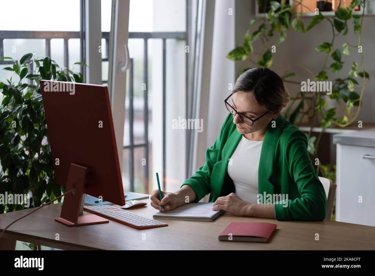 Donna caucasica focalizzata tutor o insegnante prendere appunti in notebook si siede al tavolo con il computer Foto Stock