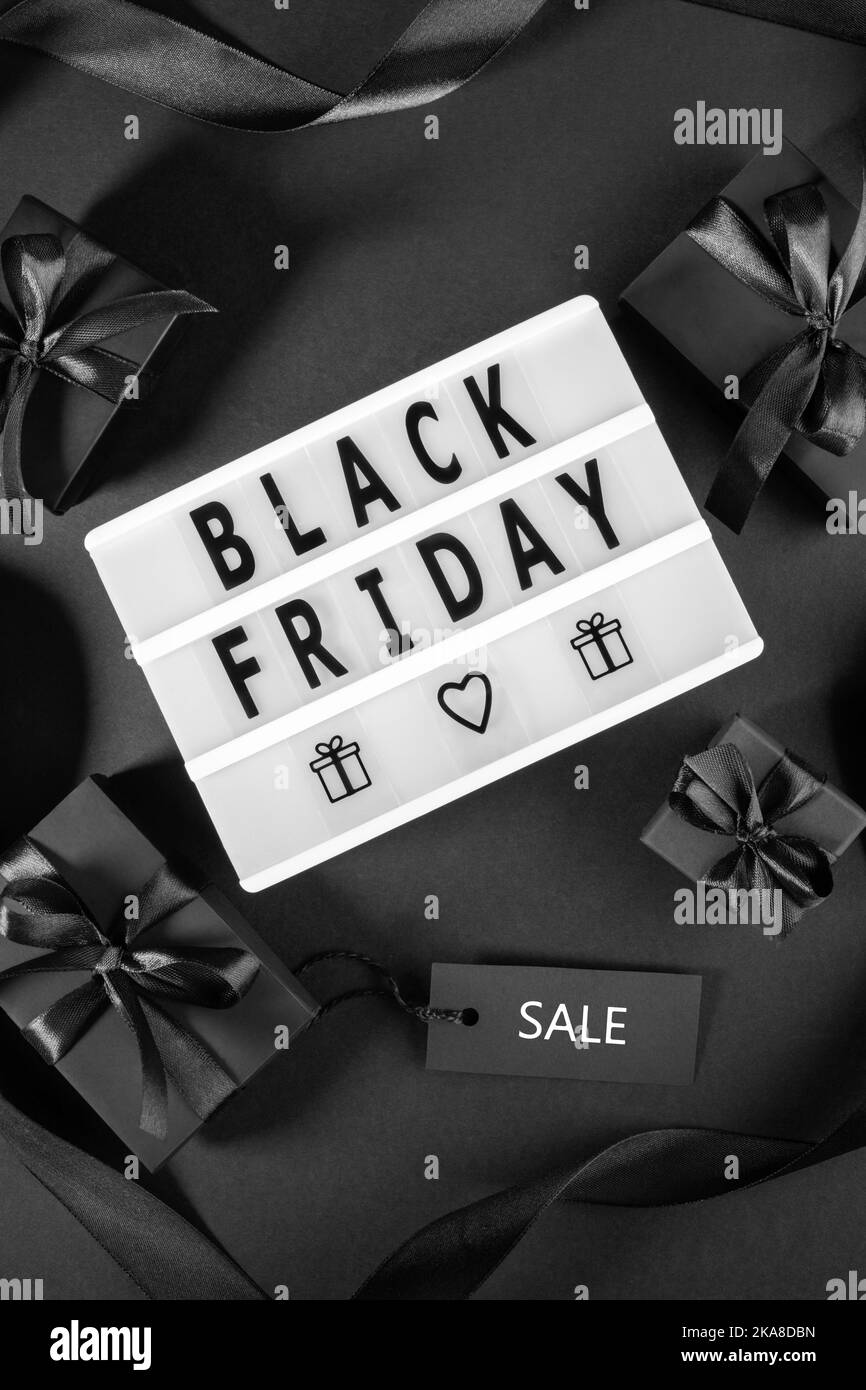 Black Friday grande vendita concetto con scatole avvolti nero nastri decorati e archi, vendita tag, scatola luminosa con lettere Black Friday su sfondo nero. Foto Stock