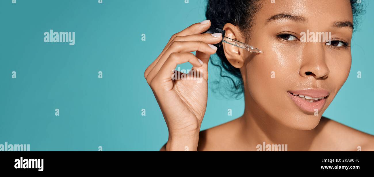 Donna africana che tiene contagocce con olio essenziale o siero vicino al viso per idratare e idratare la pelle Foto Stock