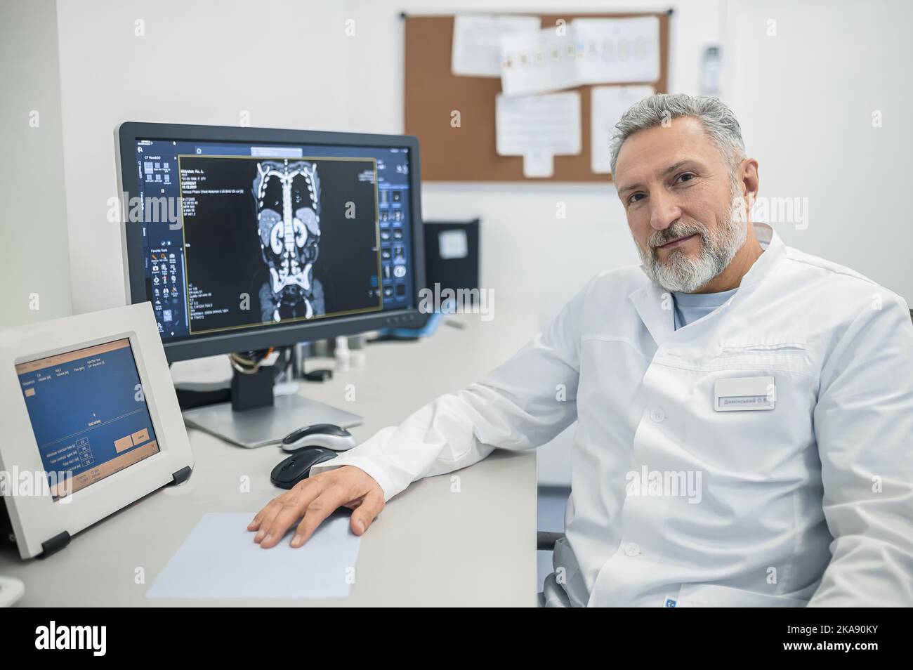 Medico dai capelli grigi in un camice da laboratorio seduto al suo posto di lavoro Foto Stock