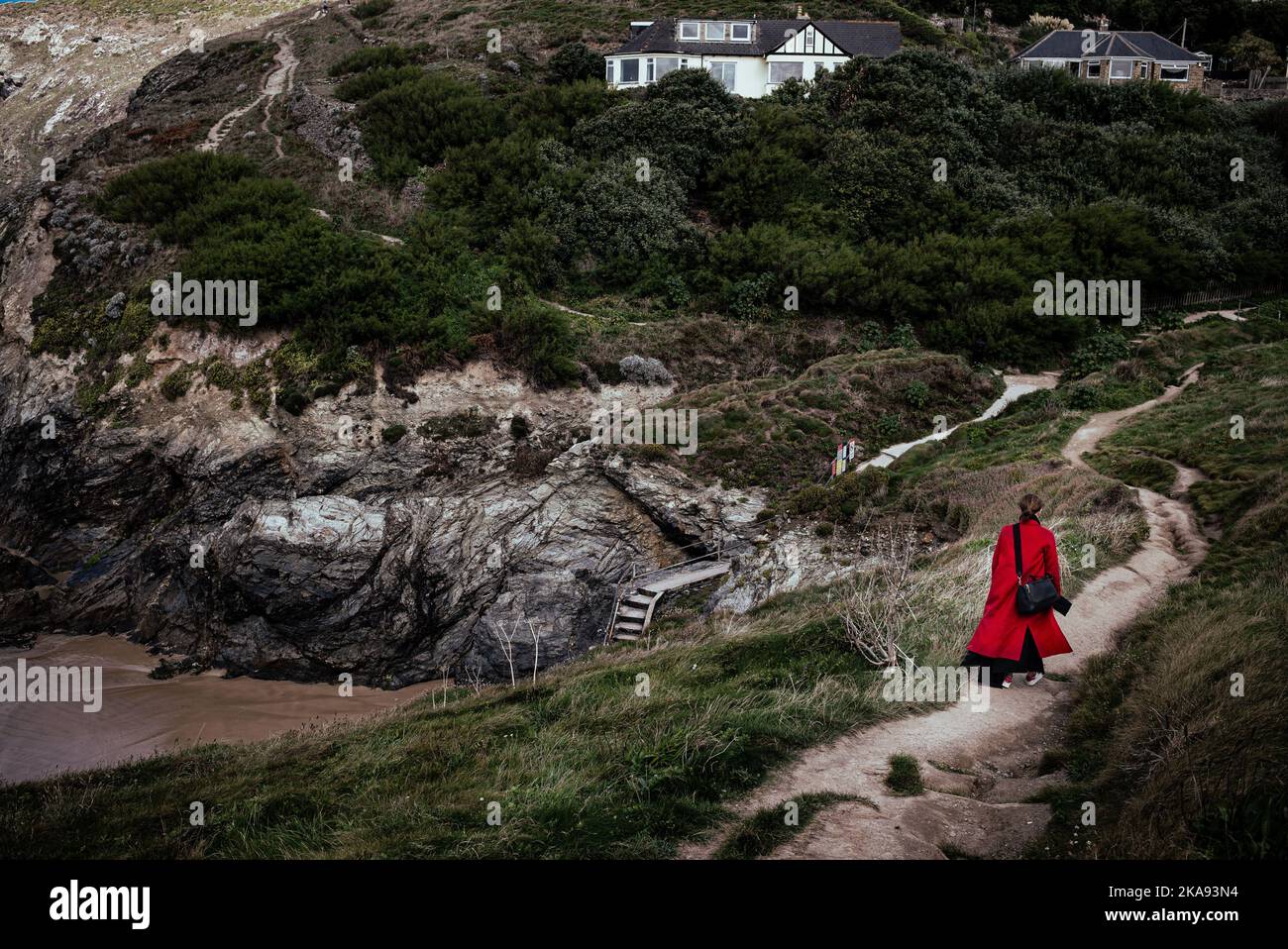 Una donna in un cappotto rosso cammina lungo un sentiero deserto in Cornovaglia, Inghilterra Foto Stock