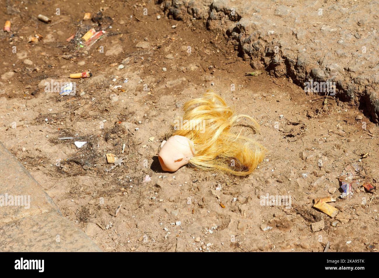 La testa di una bambola giocattolo è sdraiata in un foro del marciapiede. Foto Stock