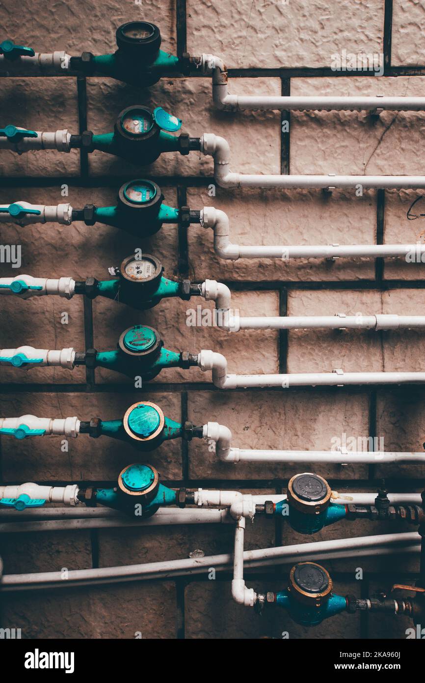 Uno scatto verticale di contatori d'acqua residenziali e tubi su sfondo muro di pietra Foto Stock