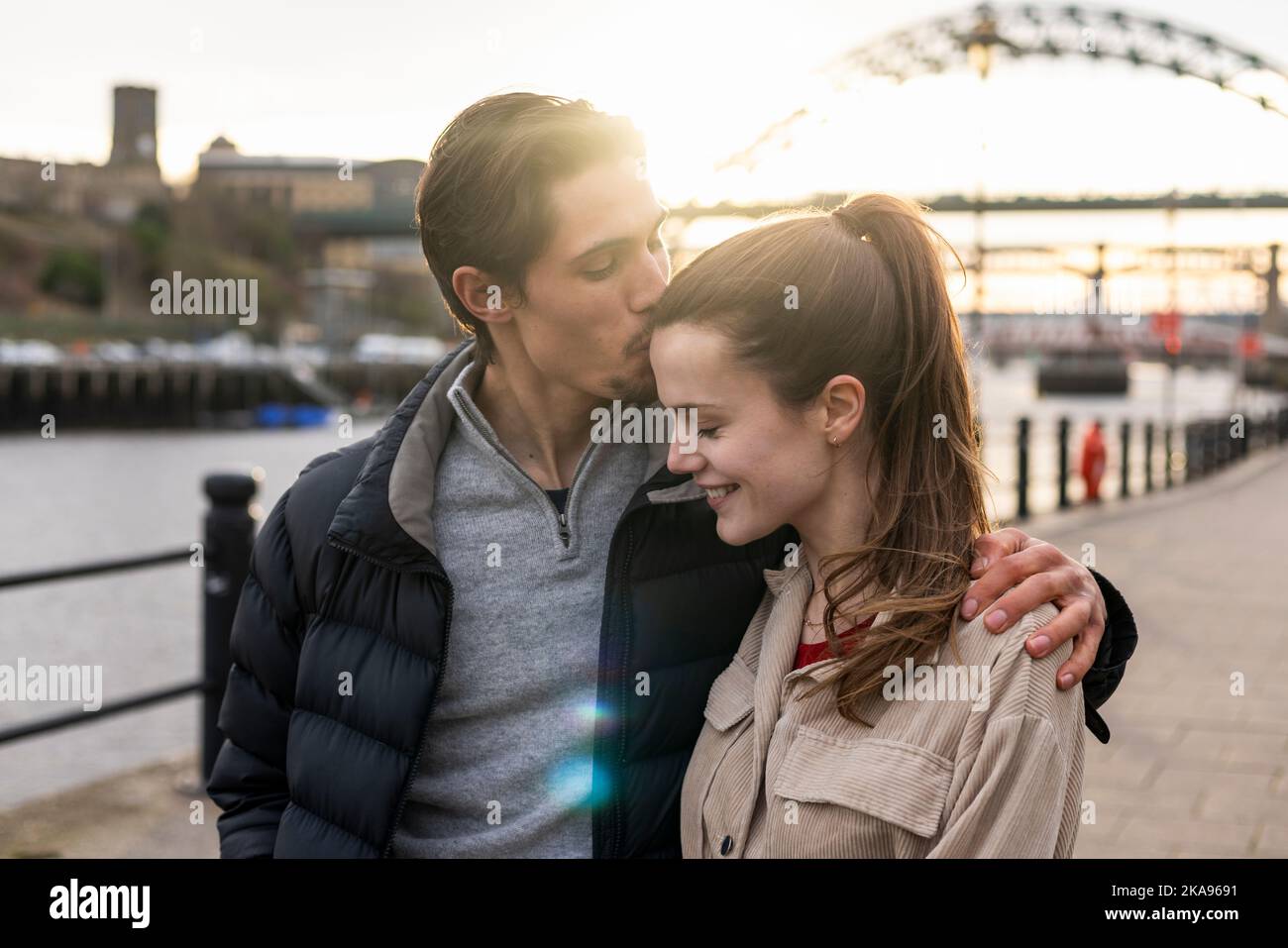 Una giovane coppia che trascorre la giornata a Newcastle upon Tyne insieme. Camminano su un passaggio pedonale lastricato lungo il fiume Tyne, abbracciandosi a vicenda Foto Stock