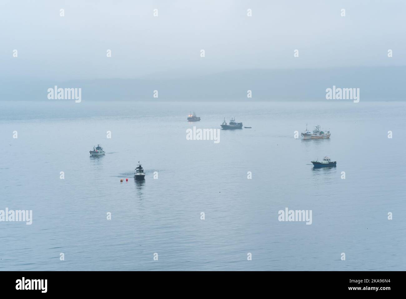 barche da pesca in mare sullo sfondo di una lontana costa nebbiosa Foto Stock