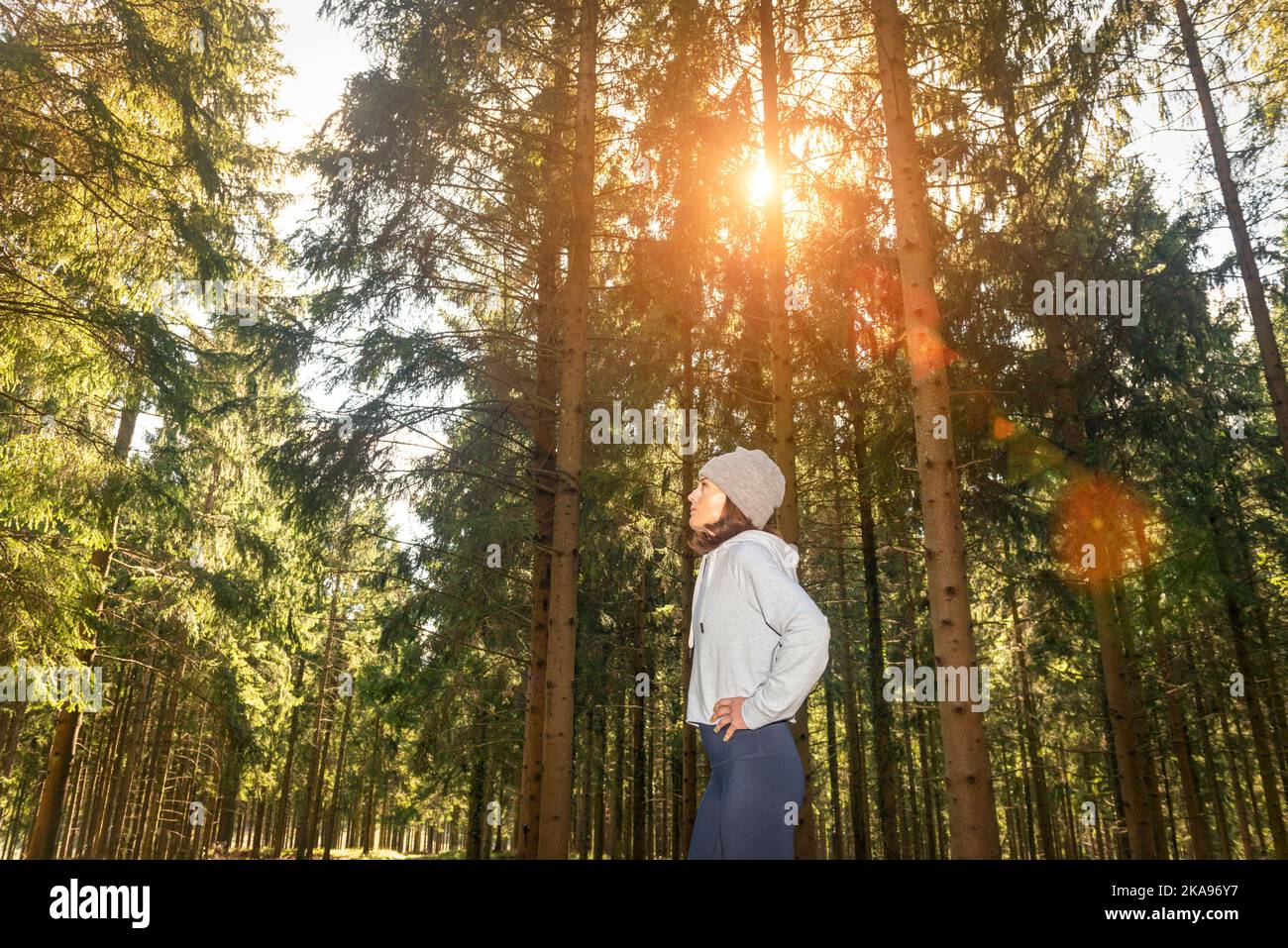 Donna sportiva in piedi con le mani sui fianchi, riposata dopo aver corso in bosco. Foto Stock