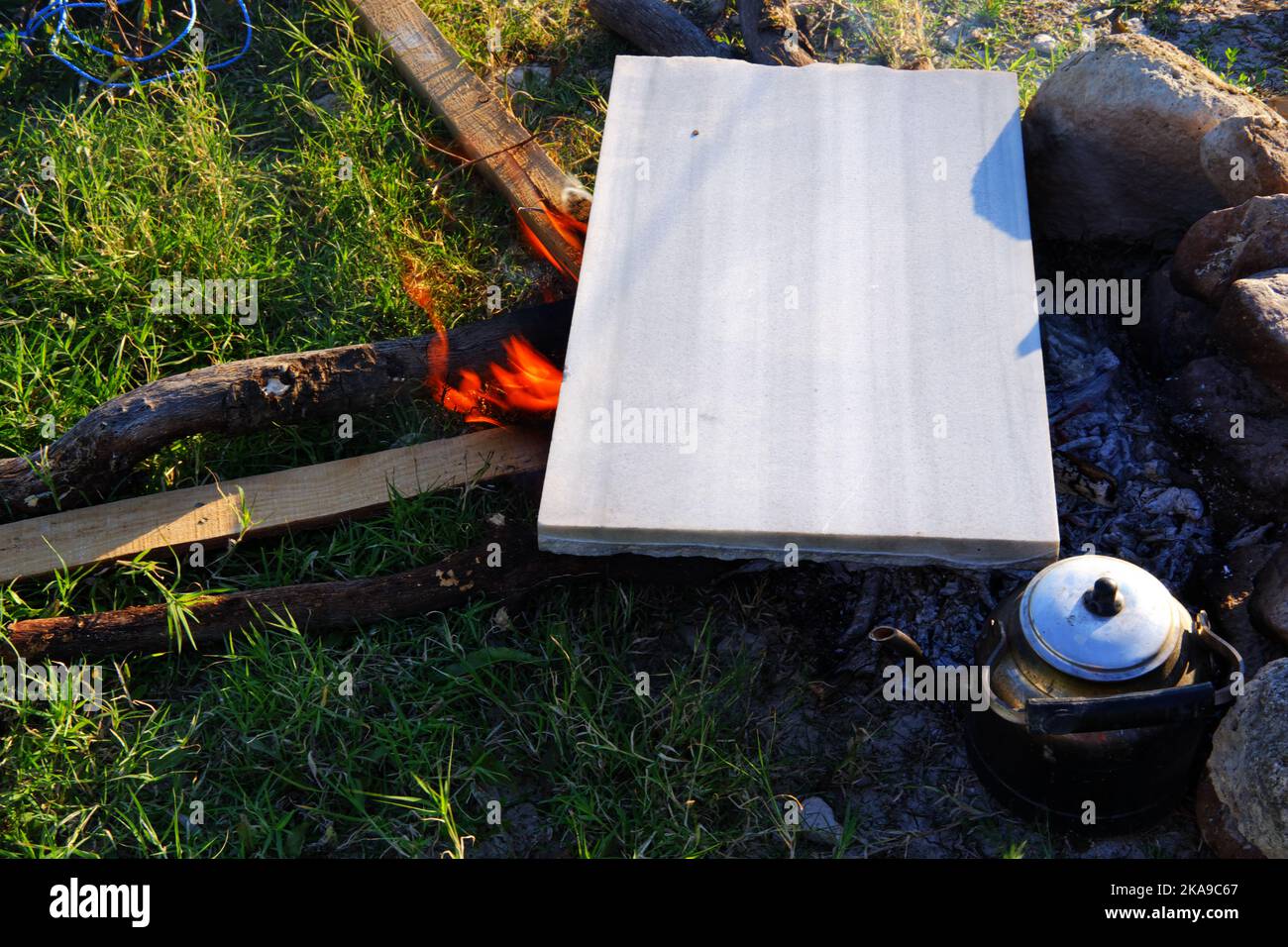 Marmo sul fuoco del campo per cucinare e teiera vicino al fuoco all'aperto in una giornata di sole estate Foto Stock