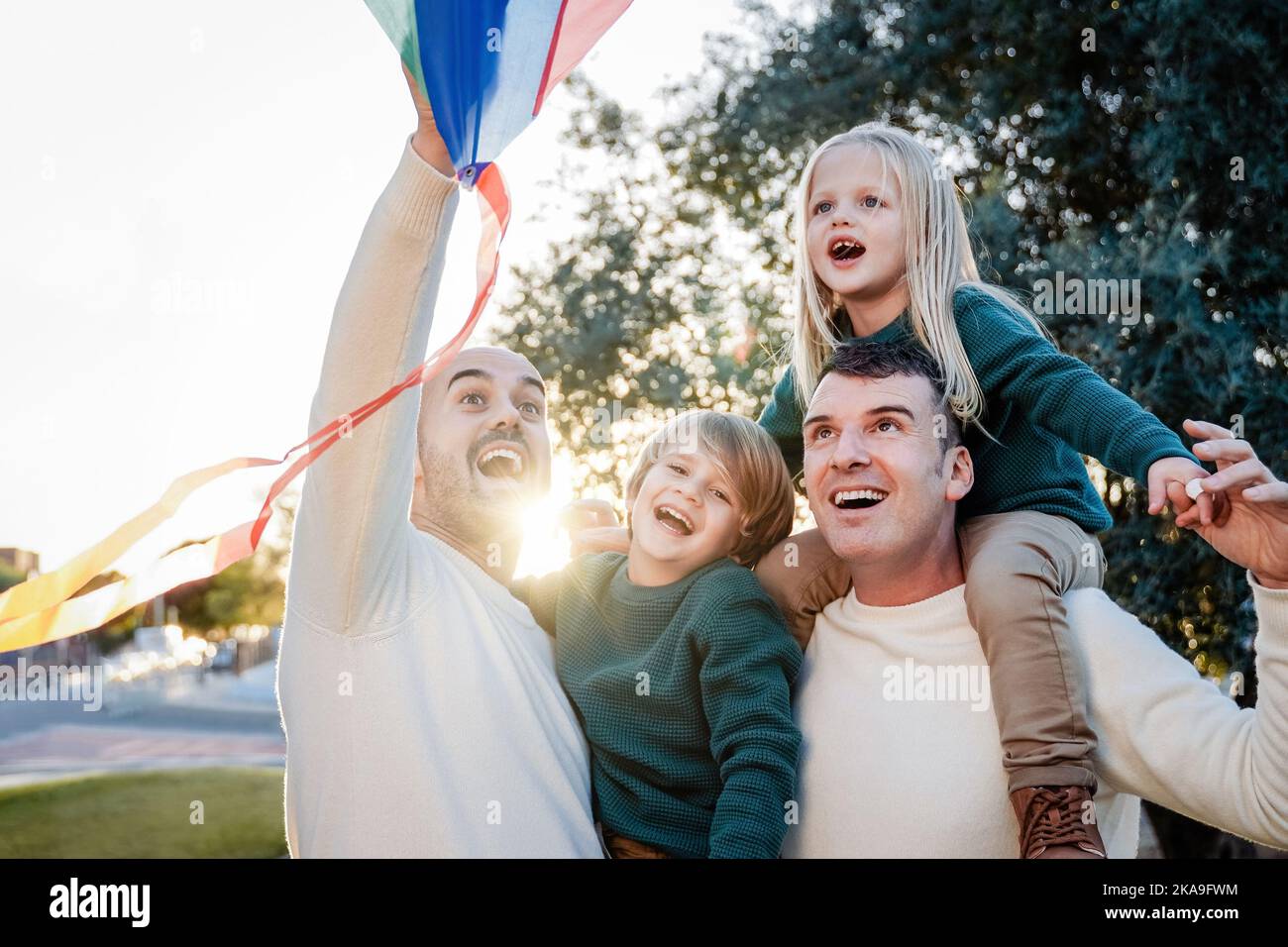 Padri gay e bambini che giocano insieme al kite all'aperto - LGBT Family Love Concept - Soft focus on right dad face Foto Stock