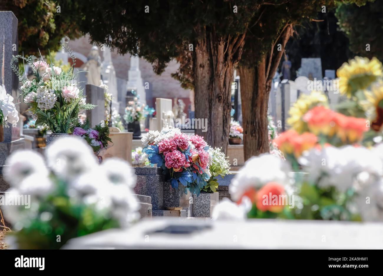 Fuoco selettivo di un mazzo di fiori di plastica su una tomba del cimitero, fuori di fuoco intorno mazzi colorati di fiori naturali, All Saints Day, Novembe Foto Stock