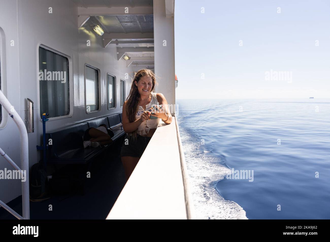 Giovane donna sorridente e che parla al telefono in un traghetto Foto Stock