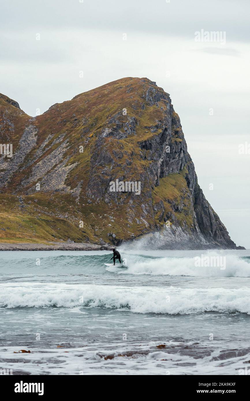 Surfista su un'onda con la montagna sullo sfondo in Unstad Lofoten Norvegia Foto Stock