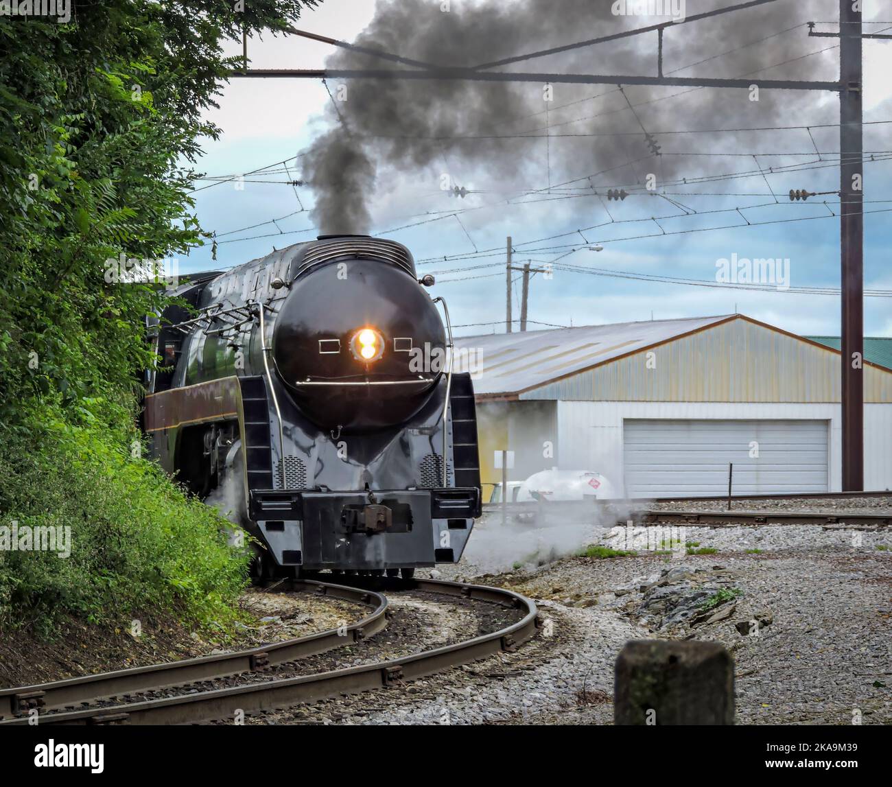 Una locomotiva a vapore che circonda una curva soffiando fumo nero e vapore bianco in un giorno d'estate Foto Stock