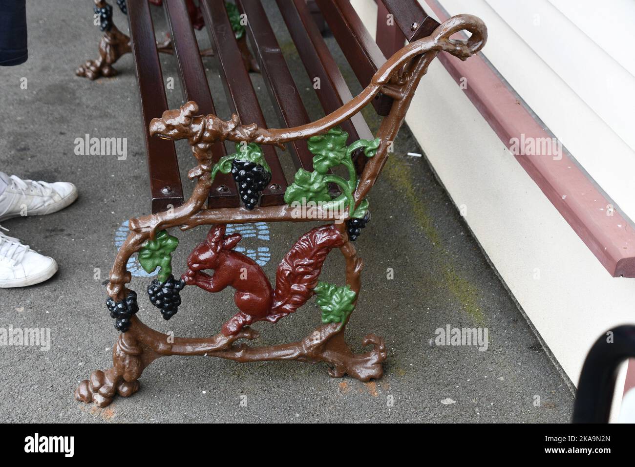 Fine di una panchina decorata in ferro dipinto raffigurante uno scoiattolo rosso che mangia uva nella stazione di Ravenglass sul Ravenglass e lo stretto di Eskdale Foto Stock