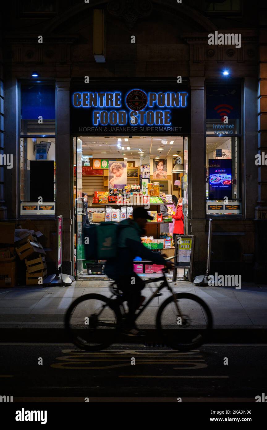 LONDRA - 3 novembre 2020: Ingresso al negozio alimentare Centre Point di notte con movimento sfocato silhouette di consegna ciclista di passaggio di fronte Foto Stock