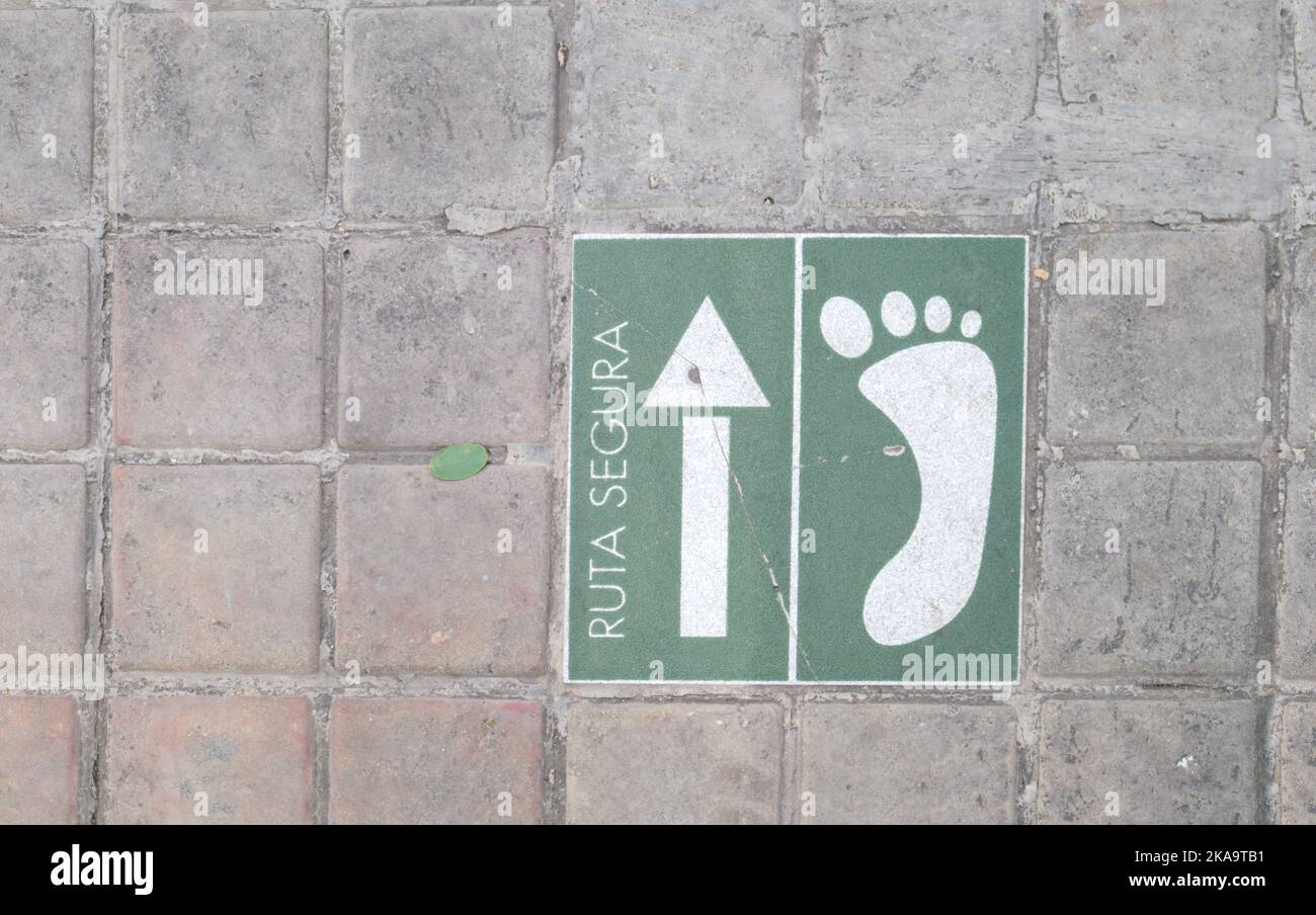 Cartello marciapiede che indica la direzione del percorso sicuro per i pedoni con una freccia e un piede disegnati in bianco su verde Foto Stock