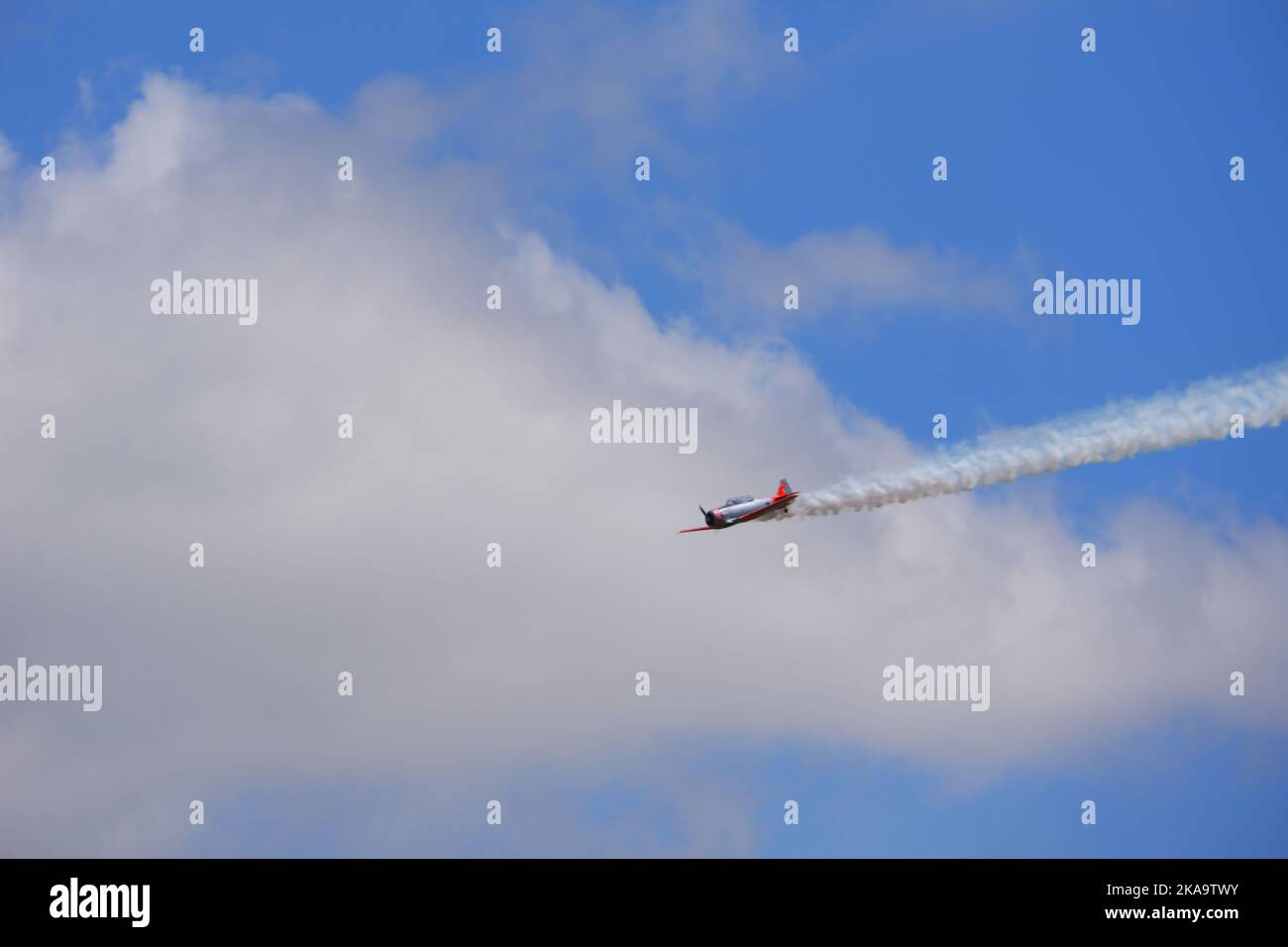 Aereo che vola con fumo sulla coda al cielo blu con le nuvole Foto Stock