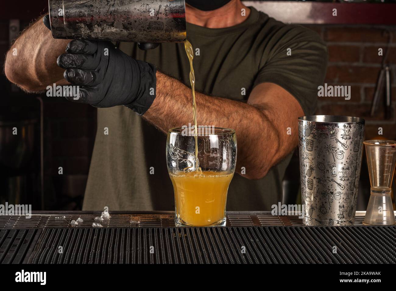 Barman al bar che beve un cocktail di alcolici in un bicchiere. Sfondo festa estiva. Foto Stock