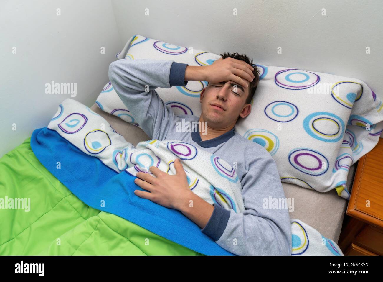 Un ragazzo caucasico malato, sdraiato nel letto di casa con la mano sulla fronte Foto Stock