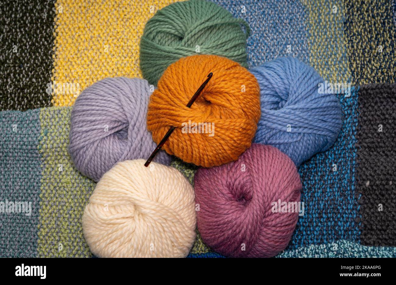 Palle di filato di lana di vari colori con ago a uncinetto, lana spessa per la lavorazione a maglia e uncinetto su fondo lavorato a maglia Foto Stock