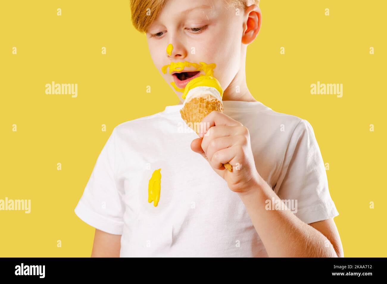 Capretto che spargerà il gelato. Rovinando i vestiti. Un ragazzo che mangia un gelato alla banana su sfondo giallo. Isolato. Concetto di colorazione della vita quotidiana Foto Stock