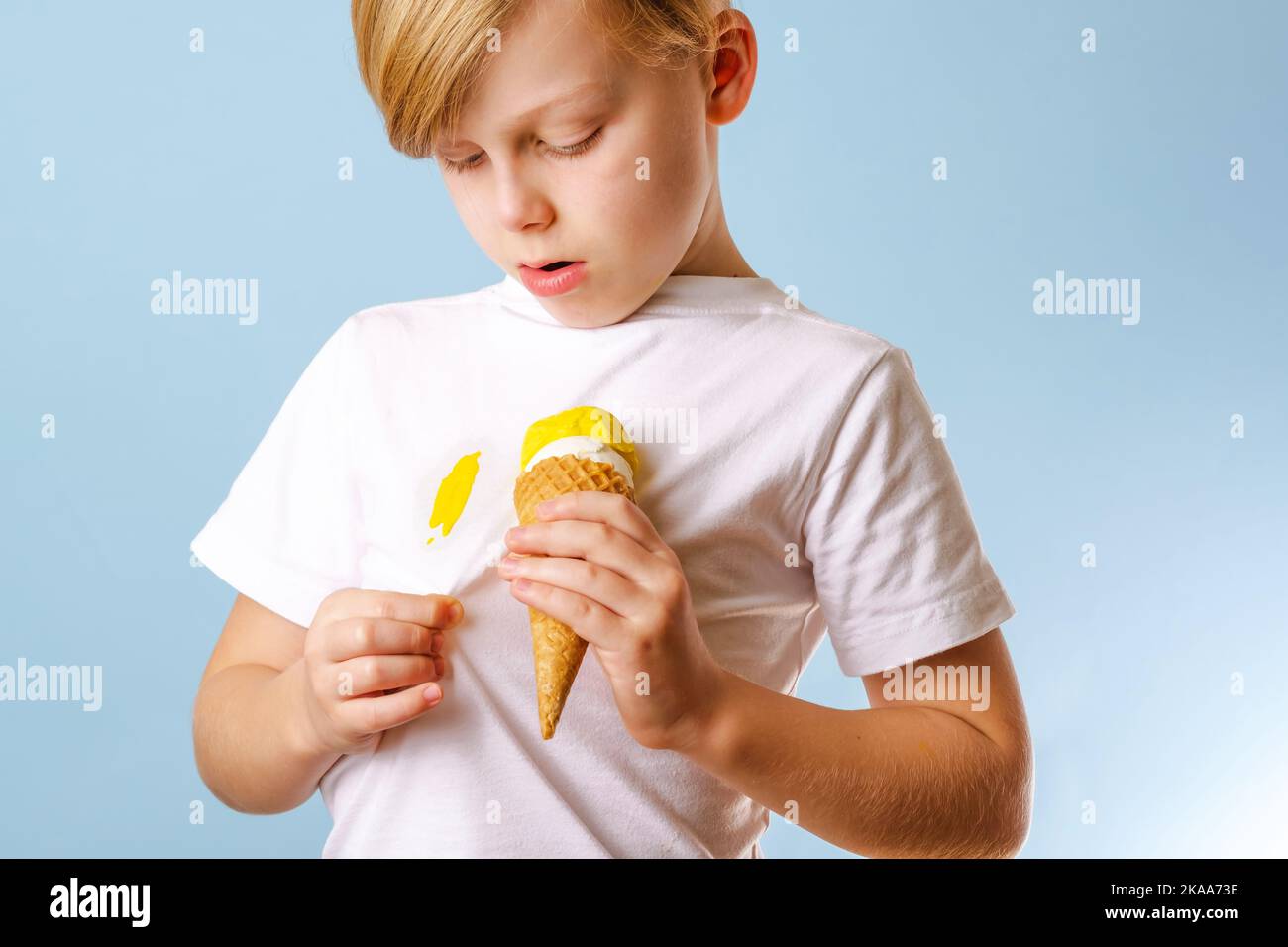 Un bambino che guarda un gelato in un cono su vestiti bianchi. Rovinando i vestiti. Isolato. Concetto di macchia di vita quotidiana. Foto Stock