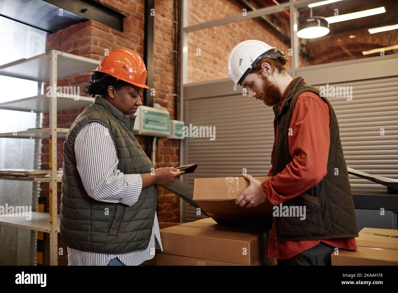 Vista laterale ritratto di due lavoratori che indossano cappelli, scatole di conteggio in fabbrica e che utilizzano tablet Foto Stock