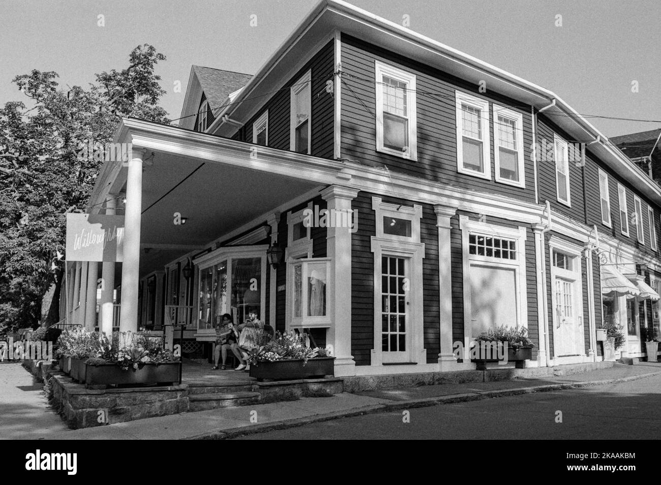 Un negozio d'epoca con una coppia di turisti che si rilassano in sedie sul poarca a Rockport, Massachusetts. L'immagine è stata acquisita in nero analogico Foto Stock