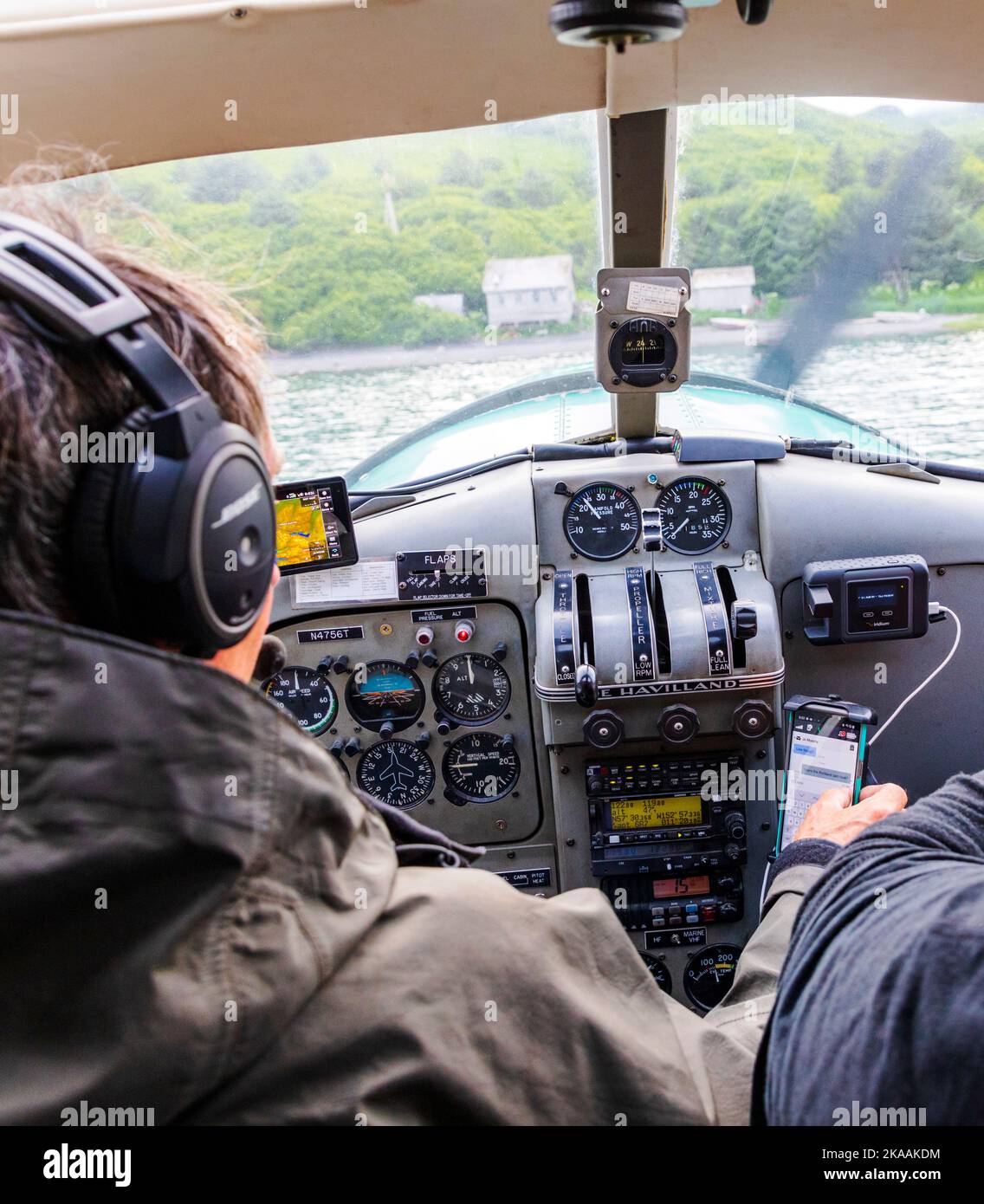 Bush pilota & guida Rolan Ruoss messaggi di testo durante l'atterraggio; Sea Hawk Air; pilotare il suo de Havilland; Beaver; float plane; Kodiak Island; Alaska; STATI UNITI Foto Stock