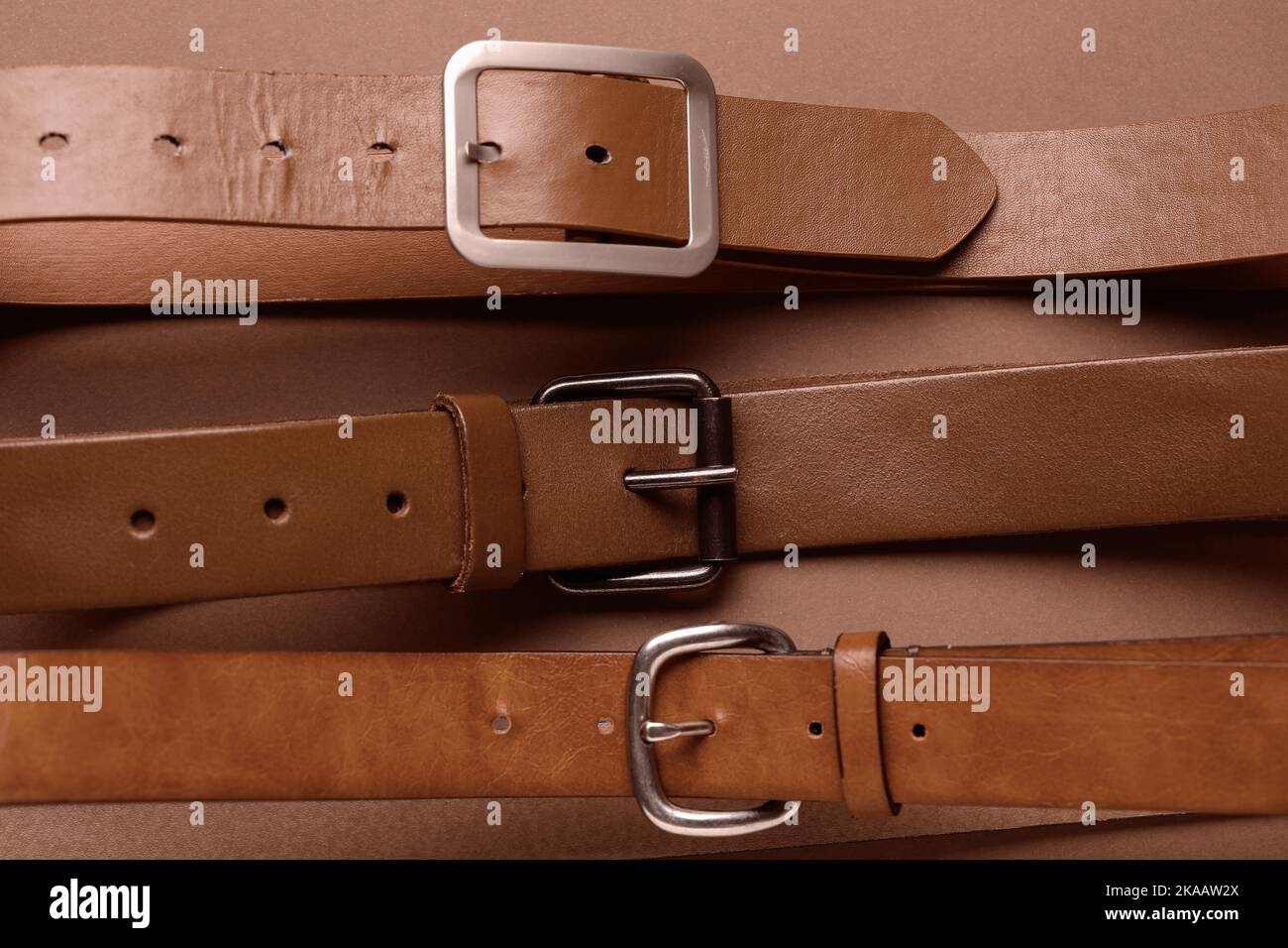 Cinture in pelle con fibbie su sfondo marrone Foto Stock