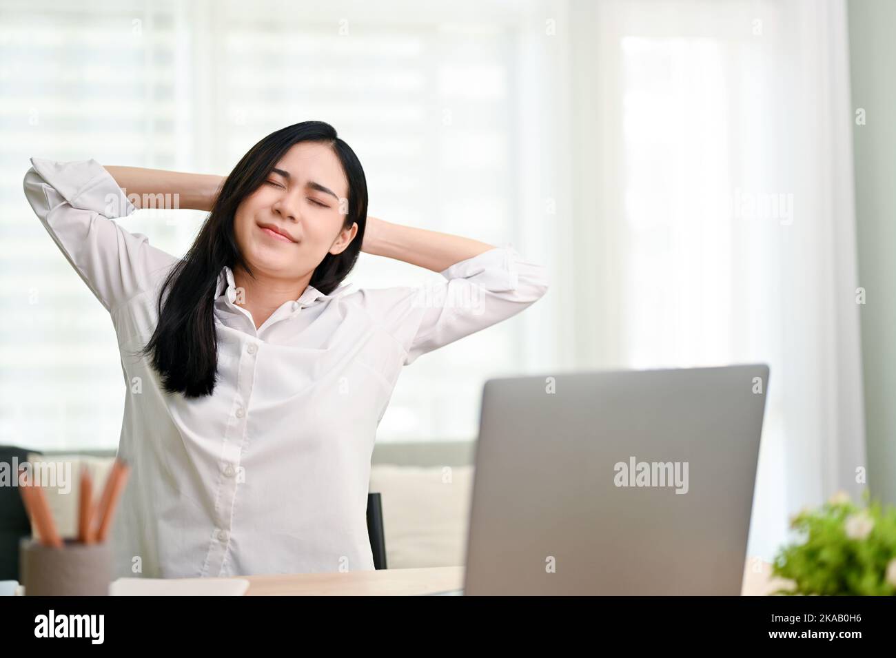 Attraente giovane donna d'affari asiatica o donne manager mani dietro la testa, gli occhi chiusi, rilassarsi alla sua scrivania in ufficio. Foto Stock