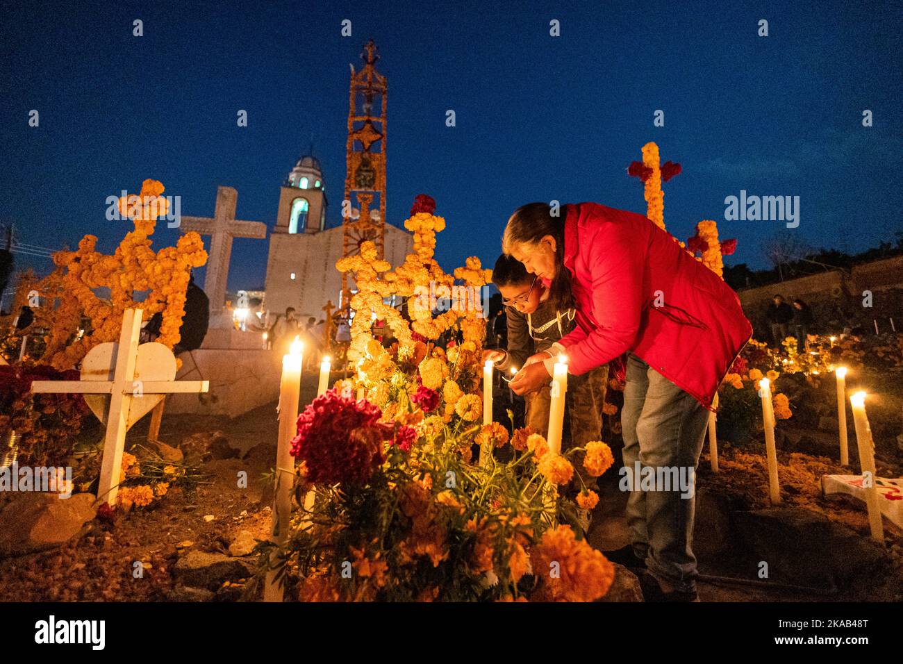 Morelia, Messico, 1 novembre 2022, le candele della madre e del figlio durante la celebrazione di giorno dei morti nel cimitero di Arocutin, Michoacan, Messico. Gli indigeni Pureecha di questo villaggio preparano questo rituale annuale del ricordo costruendo altari con marigolds, candele e il cibo o la bevanda favoriti del defunto. La veglia si svolge la notte del 1st novembre ed è diventata una grande attrazione turistica nello stato messicano centrale di Michoacan. Brian Overcast/Alamy Live News Foto Stock