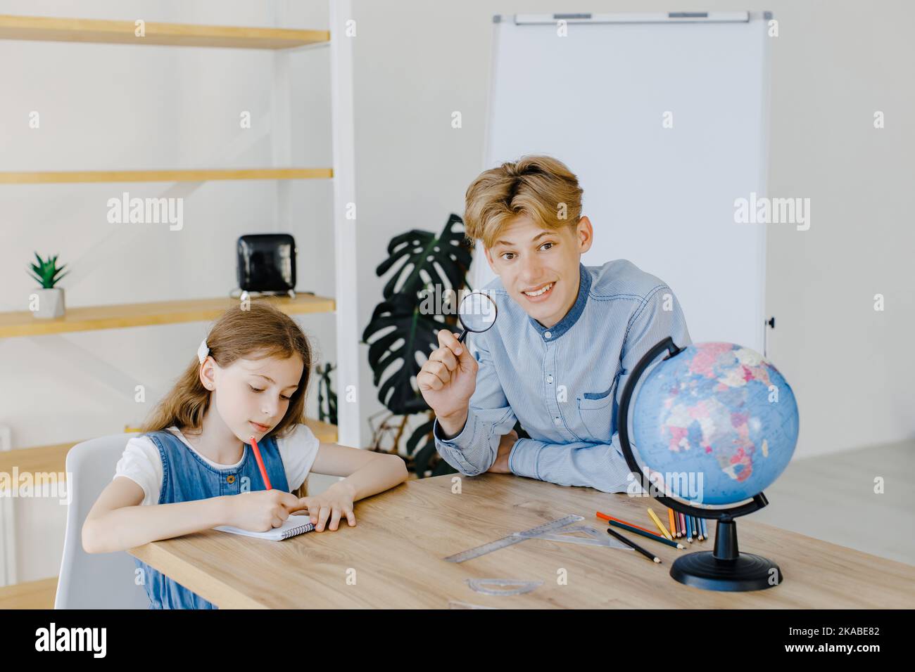 Gli allievi carini che guardano il globo in classe alla scuola. Ragazzo tenendo la lente d'ingrandimento e guardando la fotocamera Foto Stock