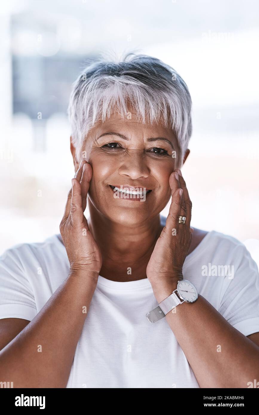 Sembra più giovane con l'età. Ritratto di una donna matura allegra che applica il makeup remover sul suo viso mentre guarda la macchina fotografica. Foto Stock