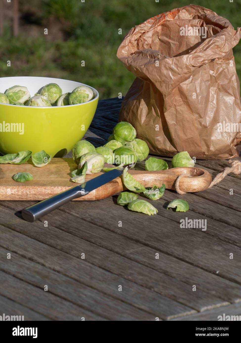 Un colpo verticale di cavoli di Bruxelles su un tagliere di legno con un coltello, un sacchetto di carta marrone e una ciotola verde Foto Stock