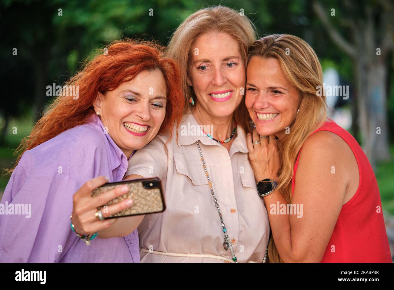 Tre donne adulte mature che prendono un selfie e che si divertono in un parco. Foto Stock