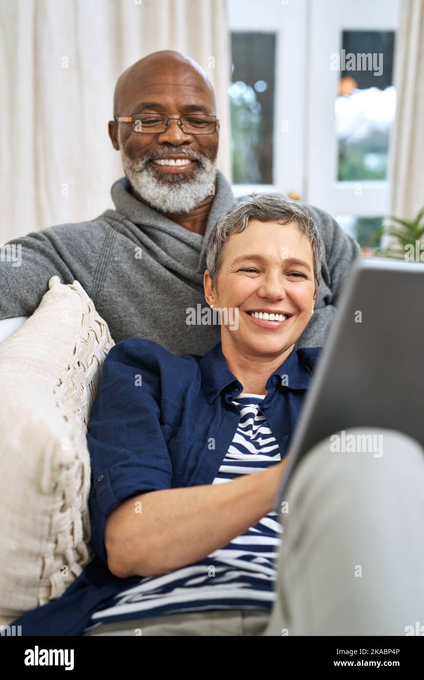 Dimostrare che l'età è solo un numero. Una coppia affettuosa senior utilizzando un tablet mentre si rilassa sul divano a casa. Foto Stock