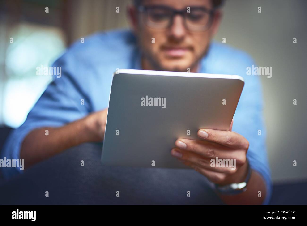 Tocca qui per l'intrattenimento. Un giovane uomo che usa un tablet digitale sul divano di casa. Foto Stock