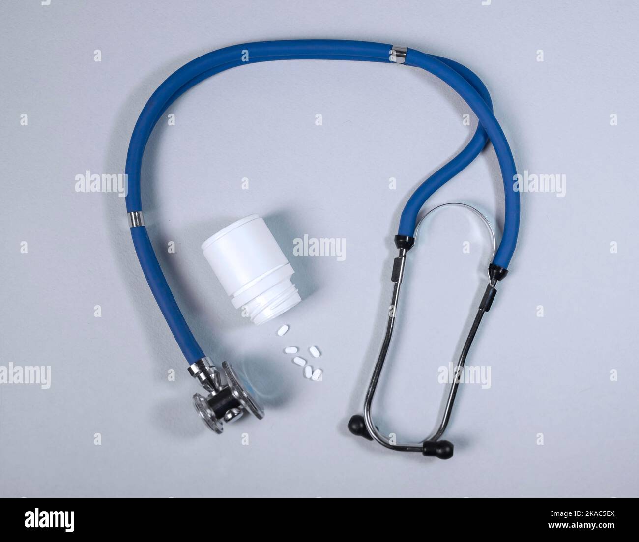 Stetoscopio e vasetto di pillole versate su sfondo grigio blu. Concetto medico. Foto Stock