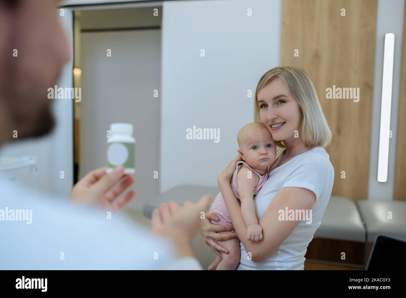 mamma bionda che parla con un pediatra maschio e tiene il suo bambino Foto Stock