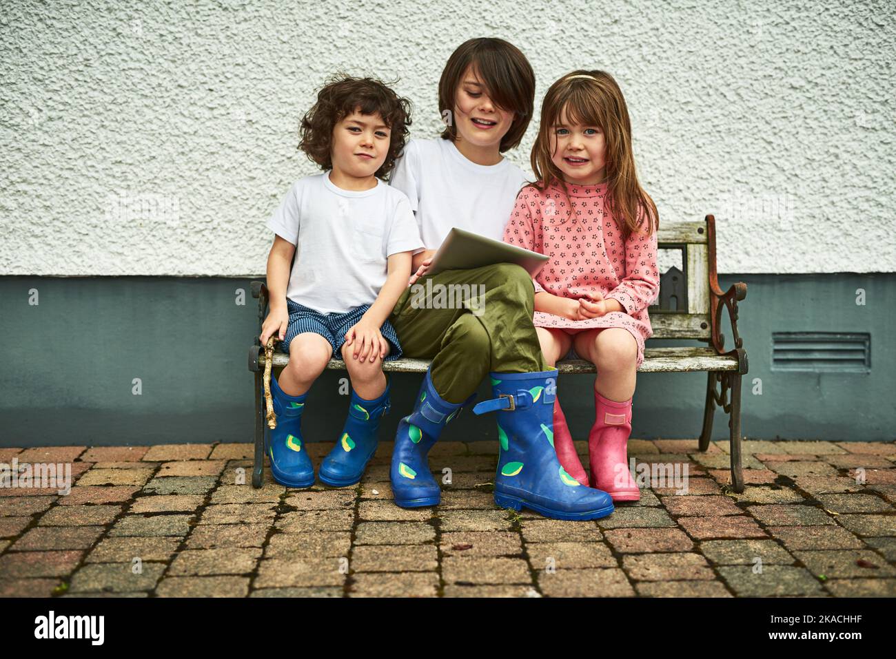 Condividere le gioie della tecnologia. Ritratto di tre adorabili bambini che usano un tablet digitale mentre si siedono su una panca all'aperto. Foto Stock