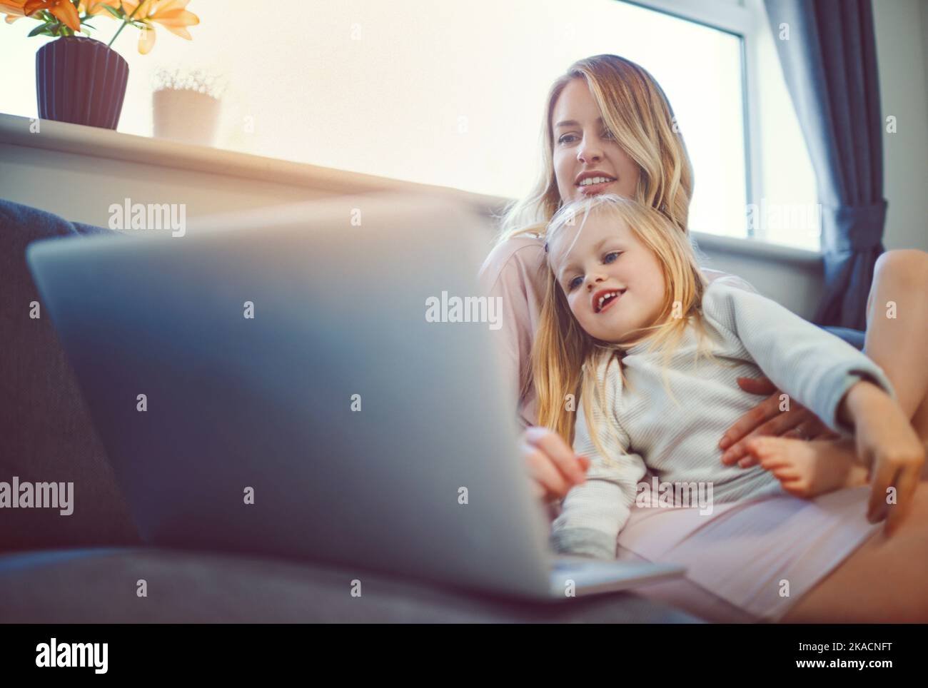 Intrattenimento per tutta la famiglia grazie alla tecnologia. Adorabile bambina che usa un notebook con la madre sul divano di casa. Foto Stock