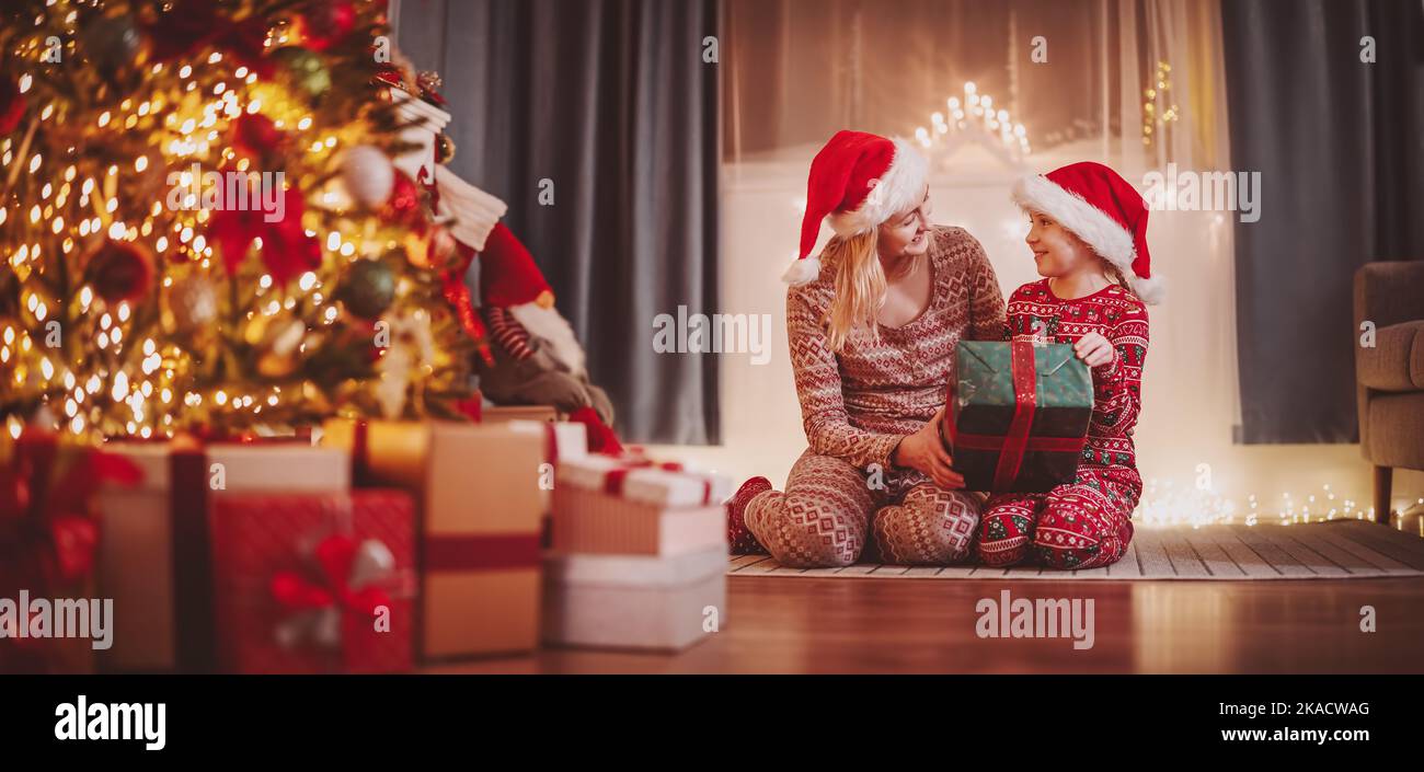 Madre e figlia seduti sul pavimento al coperto e dando presente scatola l'un l'altro nella vigilia di Natale. Foto Stock