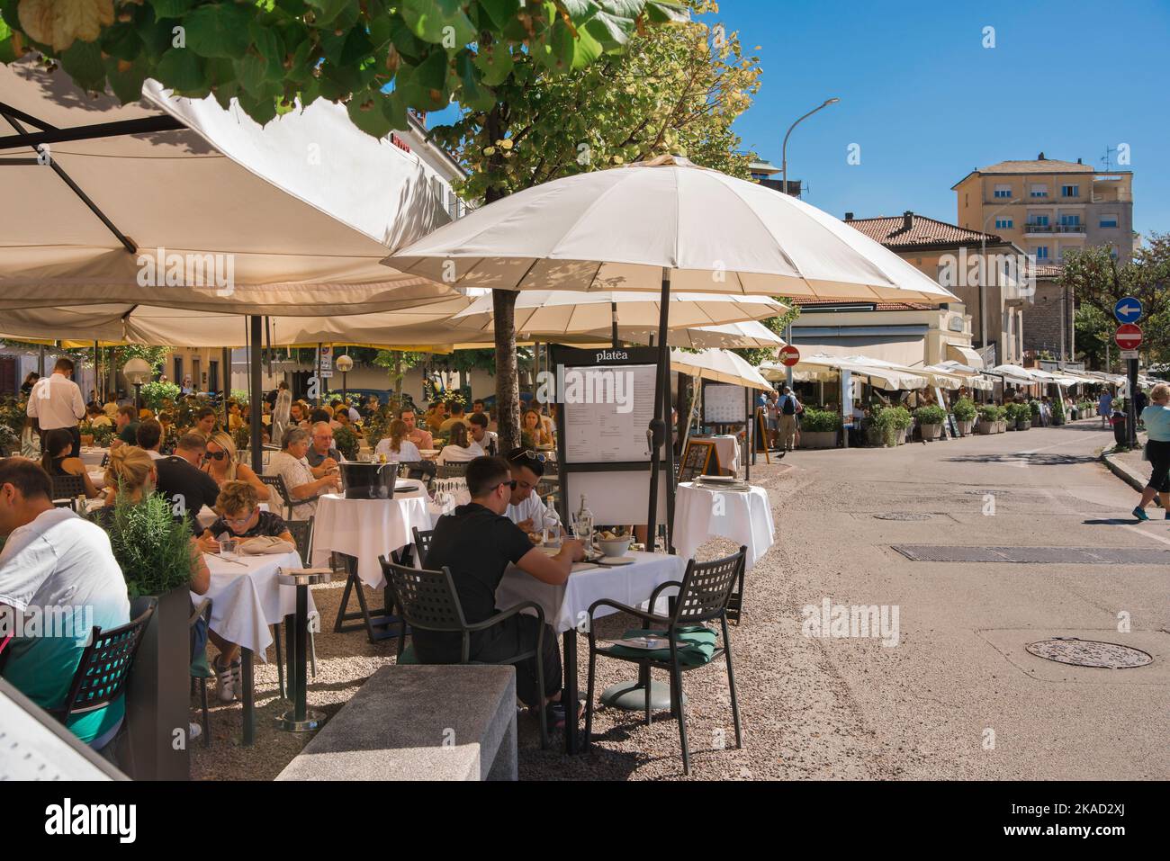 Italia food drink, vista in estate delle persone che pranzano sulle terrazze dei ristoranti lungo il bordo orientale del lago di Como nella città di Como, Lombardia, Italia Foto Stock